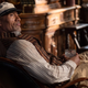 Dwayne Johnson's Jungle Cruise character Frank lounging comfortably in a chair with his legs on a table and holding a glass of alcohol.